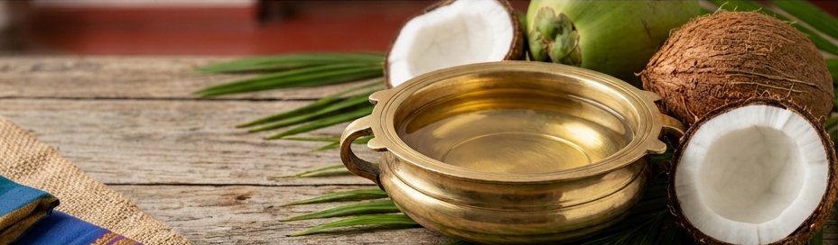 Golden coconut oil in a brass uruli surrounded by coconuts and palm fronds.